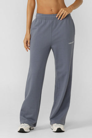 A person models the Lorna Jane Streamline Sweatpants, showing only their lower torso and legs. The relaxed-fit sweatpants feature an elastic waistband and a small logo on the upper left thigh, paired with white sneakers against a light backdrop.