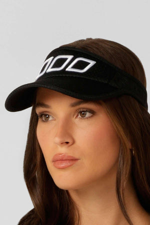 A woman with long brown hair wears the Lorna Jane Ventilation Visor, featuring breathable mesh fabric and white geometric patterns, gazing slightly to the side against a plain light background.