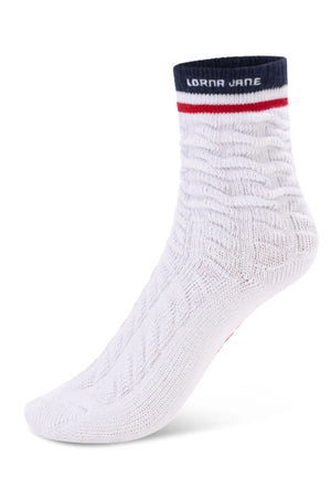 The Lorna Jane LJ Cable Knit Scrunch Socks are white with a ribbed texture, navy cuff, red stripe, and "LORNA JANE" in white at the top, shown on a foot-shaped mannequin.