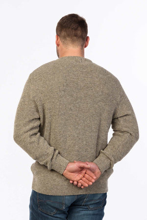 A man in an MKM Original Backyard Knit pullover and blue jeans stands with his back to the camera, hands clasped behind him, against a plain white background, embodying effortless casual wear.