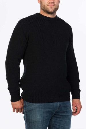 A person in a black MKM Original Backyard Knit pullover and blue jeans stands against a white background, adding a casual touch. Their short hair completes the relaxed look.