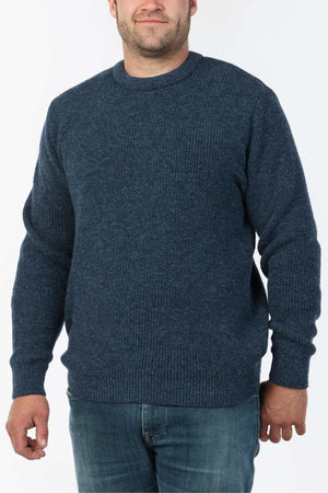 A person dons the MKM Original Backyard Knit, a blue knitted sweater with a ribbed texture and crew neckline, paired with blue jeansβa classic example of New Zealand's casual wear style against a plain white backdrop.