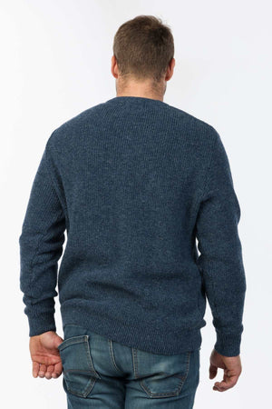 A person with short hair is seen from the back, wearing an MKM Original Backyard Knit in blue and jeans, showcasing casual wear against a plain white background.
