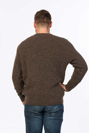 A man with short hair is standing with his back to the camera, wearing an MKM Original Backyard Knit pullover made of pure new wool and blue jeans. The background is plain white.
