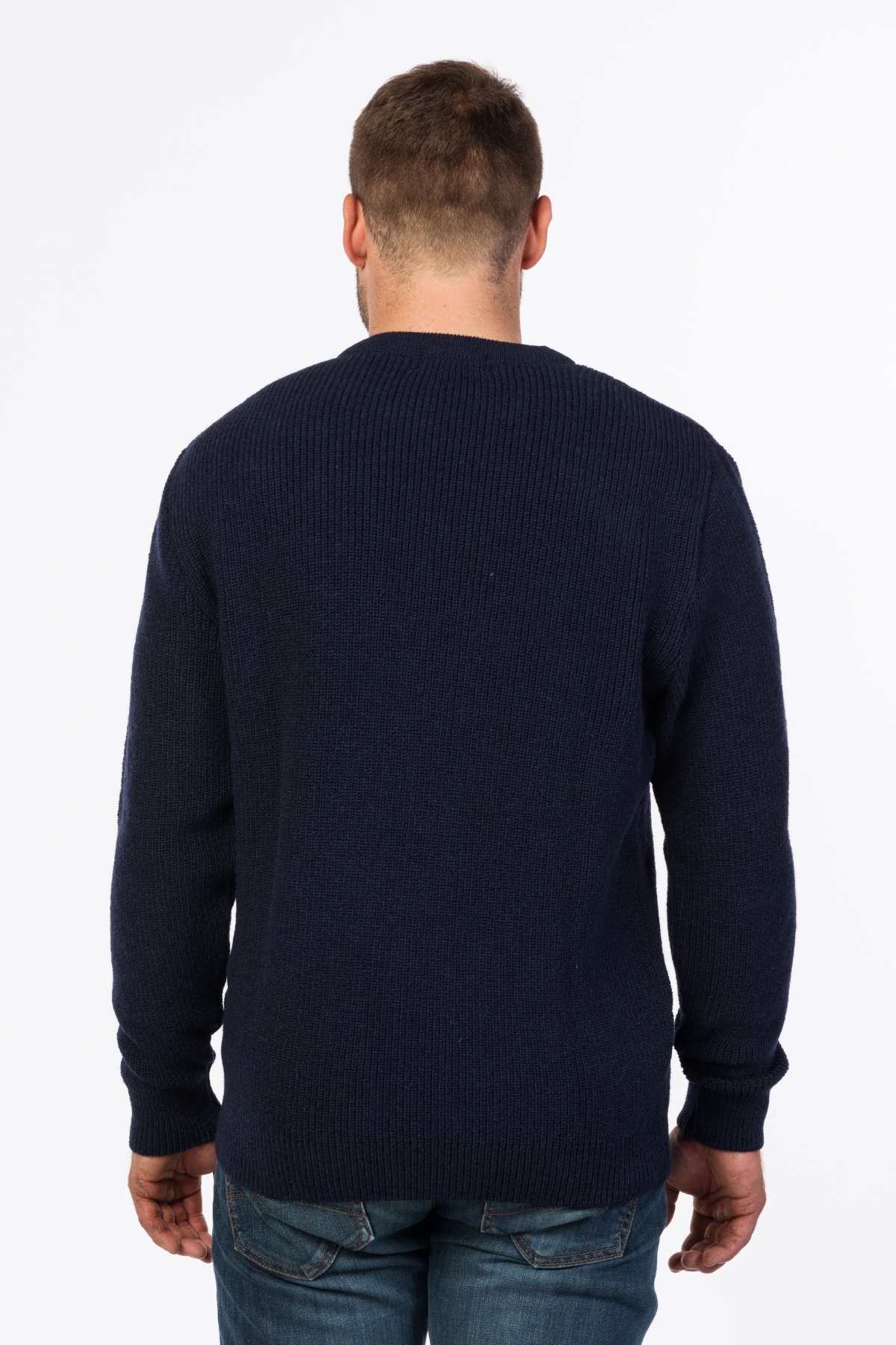 A man with short hair stands with his back to the camera, wearing the MKM Original Backyard Knit in dark blue wool and blue jeans—ideal casual wear. The background is simple and white.