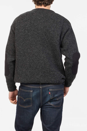 A person is shown from the back wearing a dark gray MKM Tasman Dual Layer Possum & Merino Crew sweater with black elbow patches and blue jeans against a plain white background.