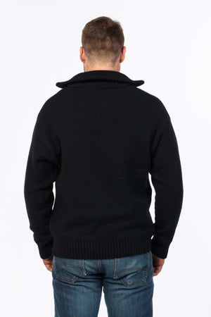 A man stands facing away, wearing a black MKM Tasman Dual Layer Possum & Merino Knit sweater with a folded collar and blue faded jeans. The background is plain white.