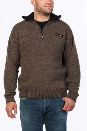 A man in an MKM Tasman Dual Layer Possum & Merino Knit, featuring a brown zip-up design with a chest logo, stands against a plain white background wearing blue jeans.