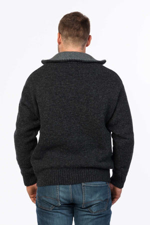 A back view of a person wearing a dark gray MKM Tasman Dual Layer Possum & Merino Knit sweater with a light gray collar, paired with blue jeans. The person has short hair and appears to be standing against a plain white background.