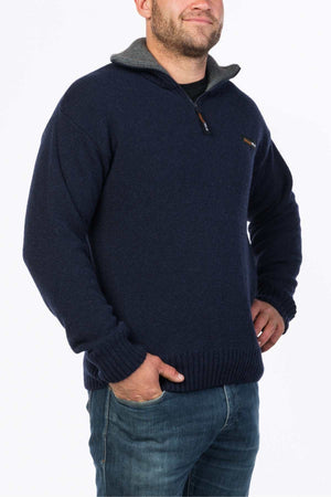 Someone wearing the MKM Tasman Dual Layer Possum & Merino Knit, a dark blue sweater with a half-zip collar, paired with blue jeans, stands against a plain white background.