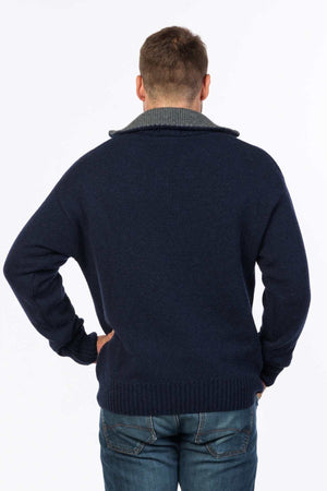 A man poses with his back to the camera in a MKM Tasman Dual Layer Possum & Merino Knit sweater featuring a gray collar, paired with blue jeans. His hands rest on his hips against a plain white background.