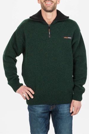 A man wearing the MKM Tasman Dual Layer Possum & Merino Knit sweater in dark green with a black collar and blue jeans stands smiling with one hand on his hip against a plain white background.
