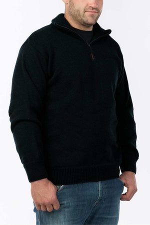 A person in the MKM Windbreaker Knitβa black, 100% wool quarter-zip sweater from New Zealandβand blue jeans stands with relaxed arms, slightly facing right against a crisp white background.