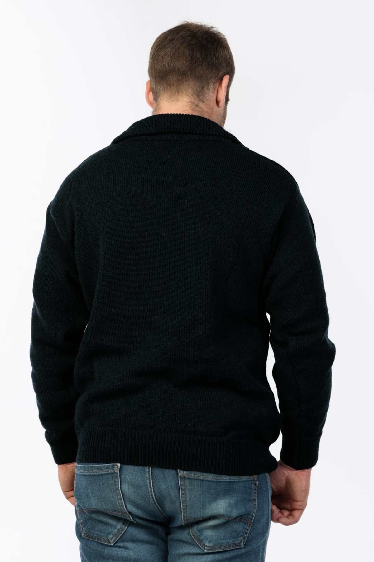 A man stands against a plain white background, facing away from the camera, wearing a dark MKM Windbreaker Knit made in New Zealand from 100% wool, paired with blue jeans.