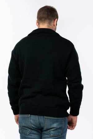 A man stands against a plain white background, facing away from the camera, wearing a dark MKM Windbreaker Knit made in New Zealand from 100% wool, paired with blue jeans.