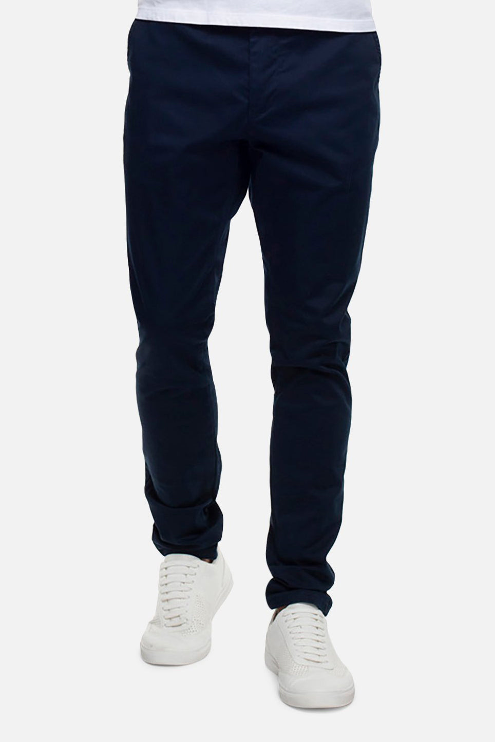 A person wearing dark blue Industrie The Cuba Chino Pants and white sneakers is shown from the waist down against a plain background. The slim-fit chinos paired with the simple, clean design of the white-laced sneakers exude a relaxed yet stylish vibe.