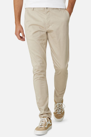 Wearing the Industrie The Cuba Chino Pant in light beige with white sneakers, a person strides forward against a plain white background, highlighting the casual style of their lower body and legs.