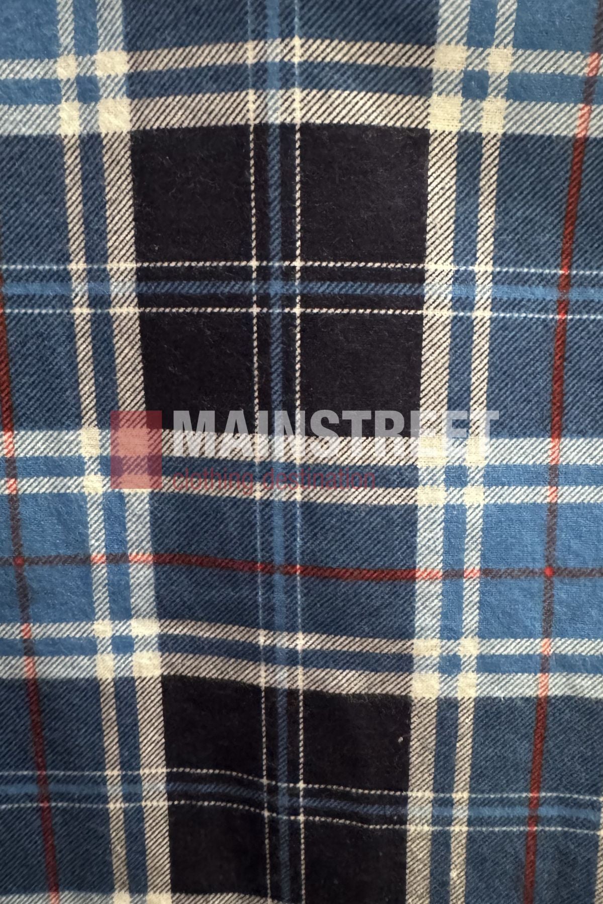 A blue, white, and black plaid pattern with thin red lines forms the classic tartan design of the Milton Open Front Flannelette Shirt. "MAINSTREET" is faintly visible across the center.