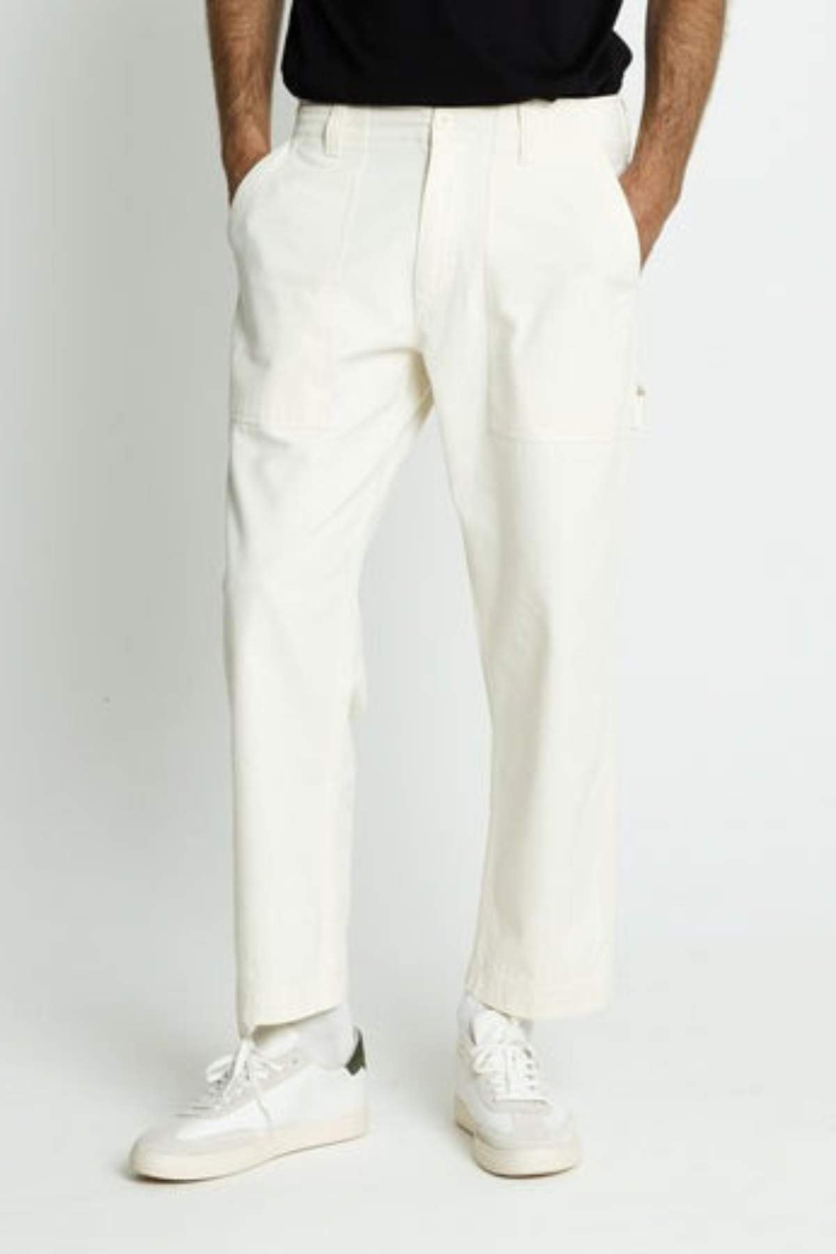 A person wearing off-white Mr Simple Carpenter Pant in a relaxed fit, hands in pockets, paired with white sneakers and a black shirt. The image is cropped at the chest, so the face is not visible.