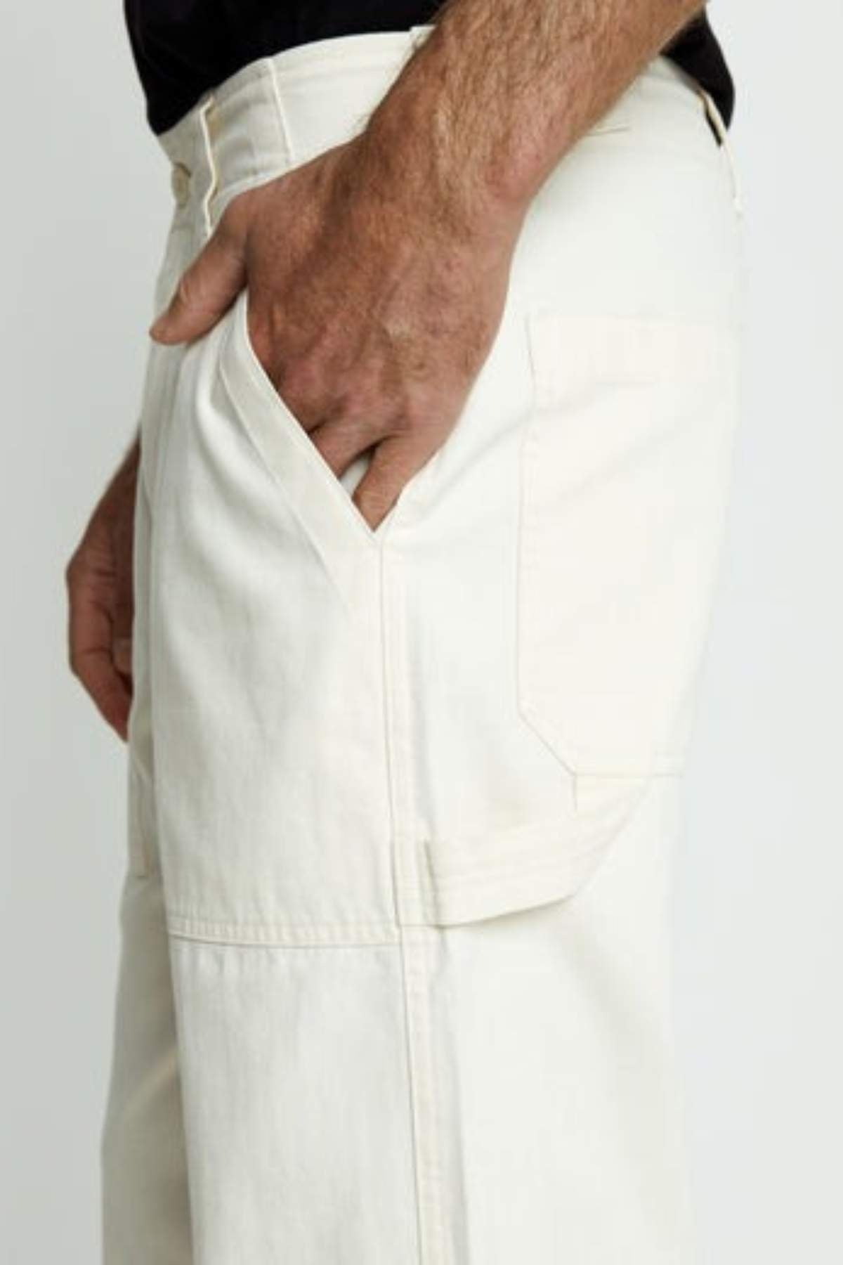 A person wears light-colored, relaxed fit Mr Simple Carpenter Pant with their right hand in the front pocket, shown waist to knee against a plain background.