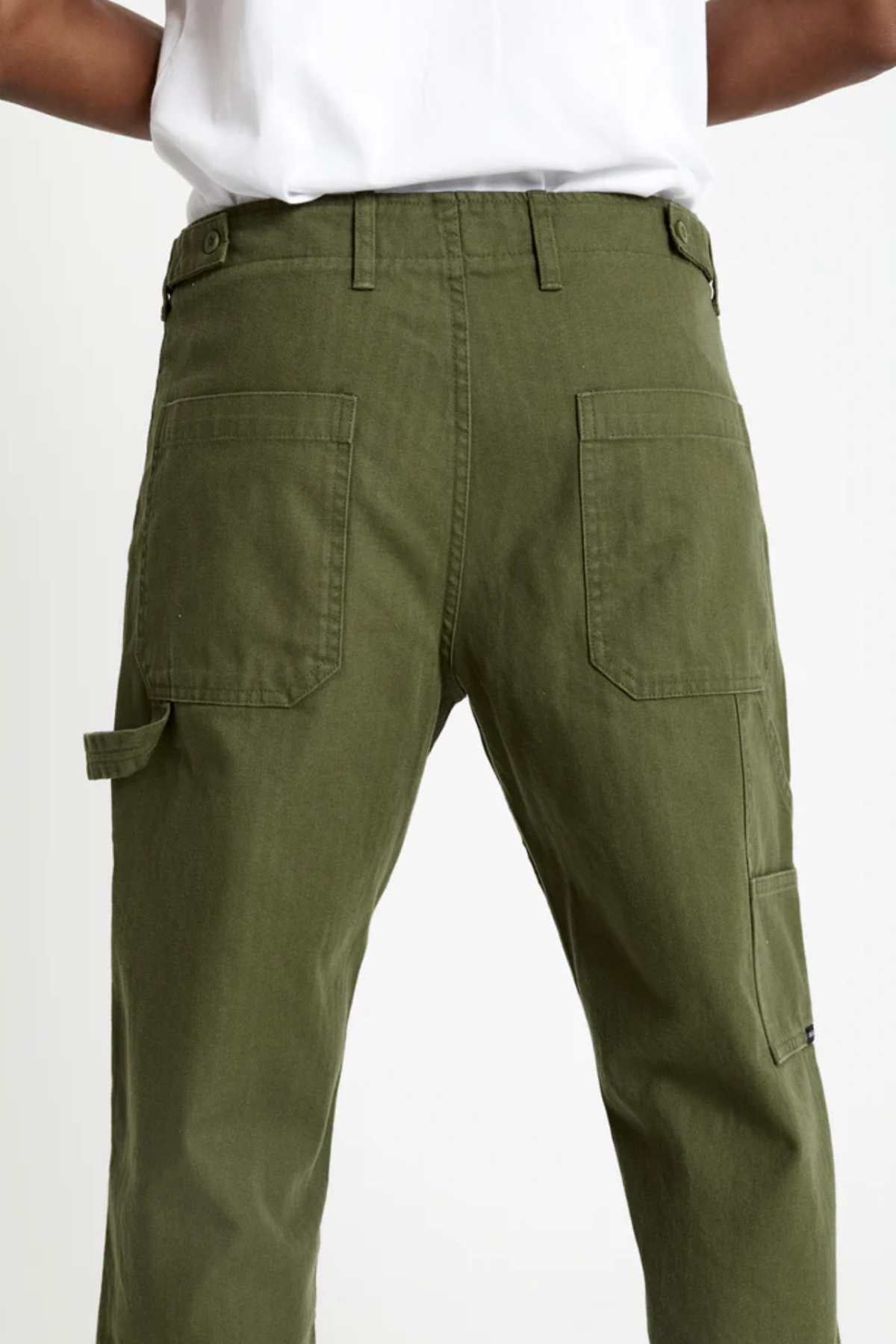 Model wears Mr Simple Carpenter Pant in olive green, featuring a workwear-inspired design and back patch pockets, paired with a white shirt. Shown from the waist down, facing away from the camera.