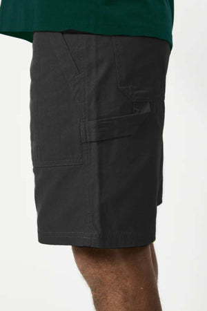 Someone is wearing the Mr Simple Carpenter Walk Short, featuring multiple pockets and a dark Herringbone Cotton with a relaxed fit, paired with a green top against a plain background.