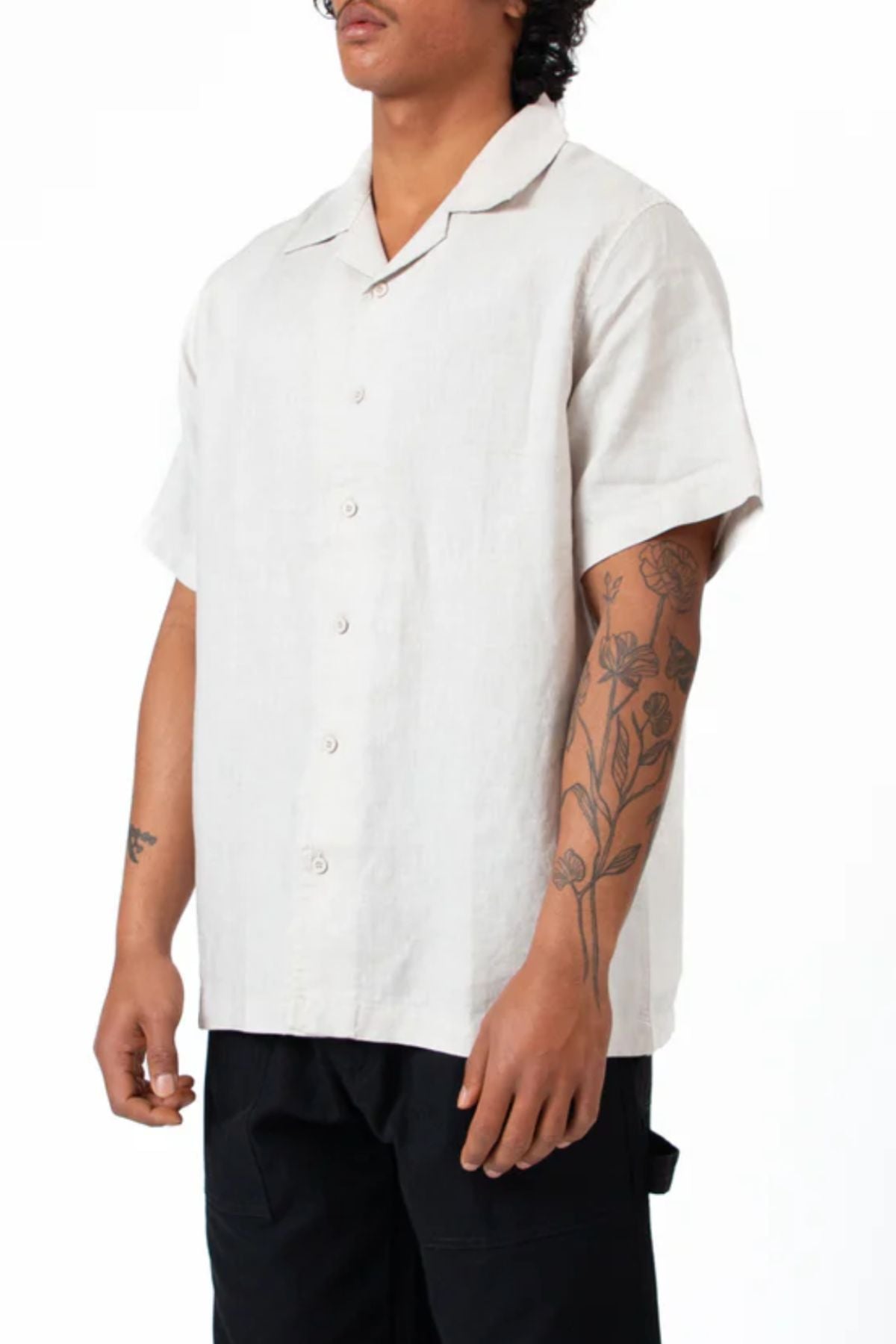 Wearing the Mr Simple Cuban Short Sleeve Shirt in a relaxed fit and light color, paired with black pants, a person with floral forearm tattoos stands against a plain white background.