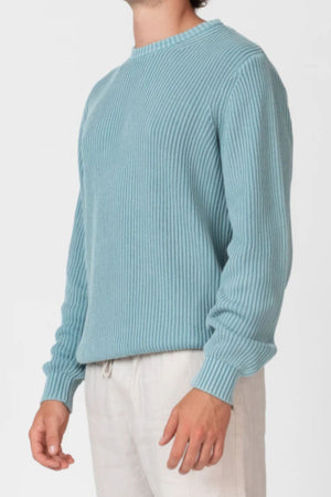 A person wears the Mr Simple Fisher Knit sweater in light blue (relaxed fit, long sleeves) with off-white pants, standing against a plain light background. Their head is partially out of frame.