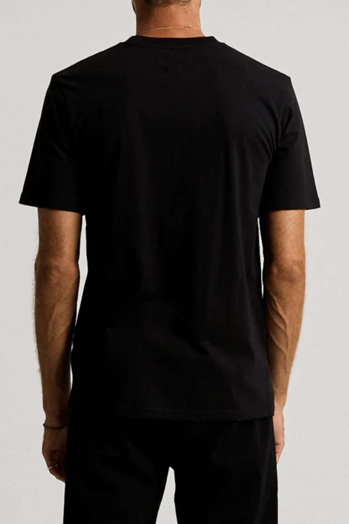 A person stands with their back to the camera, wearing the Mr Simple Heavy Weight Tee—crafted from 100% organic cotton in a boxy fit—paired with black pants, set against a neutral background.
