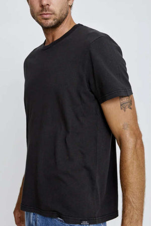 Wearing the Mr Simple Hemp Tee in plain black and blue jeans, a man shows his right forearm tattoo against a neutral light gray backdrop, subtly highlighting his sustainable attire.