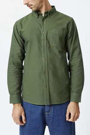 A person in a Mr Simple Oxford Shirt, a slim-fit button-up crafted from organic cotton with a left chest pocket, paired with blue jeans, stands against a plain white background looking to their right.