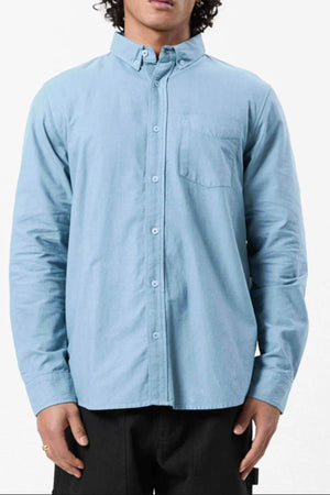 A person wearing the Mr Simple Oxford Shirt in light blue, a slim-fit 100% cotton shirt with a front pocket, stands against a plain white background.