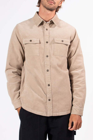 A man stands with one hand in his pocket against a plain white background, wearing the Mr Simple Quilted Cord Jacket—a beige, quilted cord jacket with snap closure and two chest pockets.