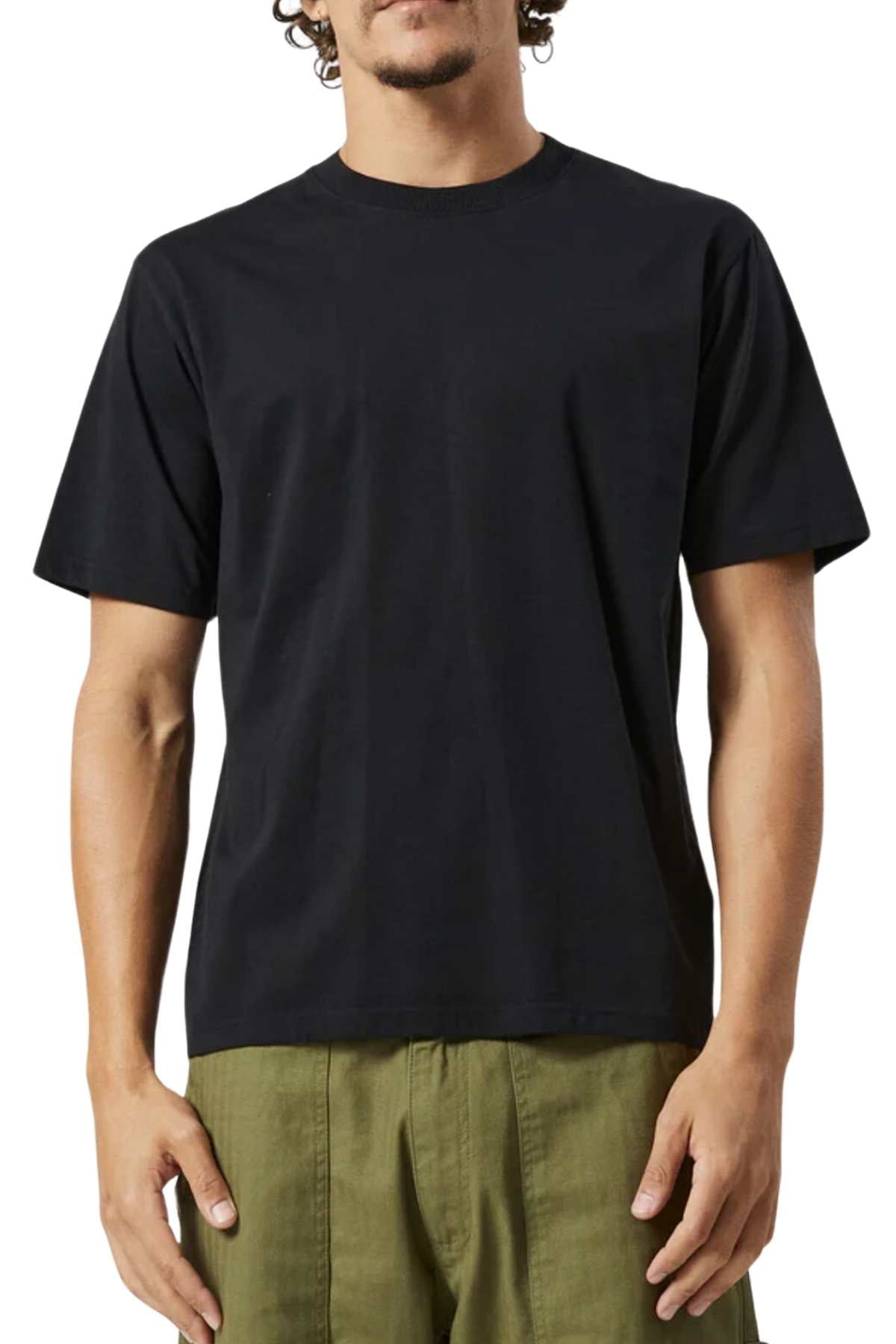 A person with short, curly hair is shown from the neck down wearing a plain black Mr Simple Reginald Organic Tee and olive green pants. The individual is standing against a white background with their arms relaxed by their sides.
