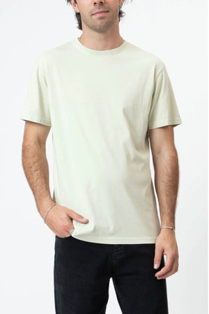 A person wearing the Mr Simple Reginald Organic Tee in light beige and black jeans stands against a white background, with one hand in their pocket.