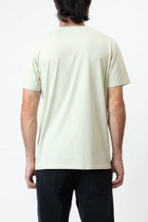 A person with dark hair is shown from the back, wearing the Mr Simple Reginald Organic Tee in a comfortable fit and light color, paired with dark pants, standing against a plain white background.