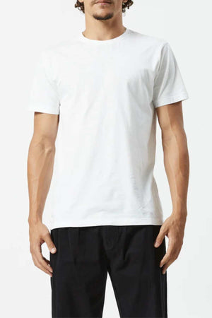 Someone stands against a white background, arms relaxed at their sides, wearing the Mr Simple Reginald Organic Tee—plain white, made from 100% organic cotton—and black pants.