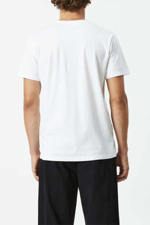 A person with short curly hair is shown from the back wearing the Mr Simple Reginald Organic Tee, a plain white 100% organic cotton midweight shirt, paired with black pants against a light background.
