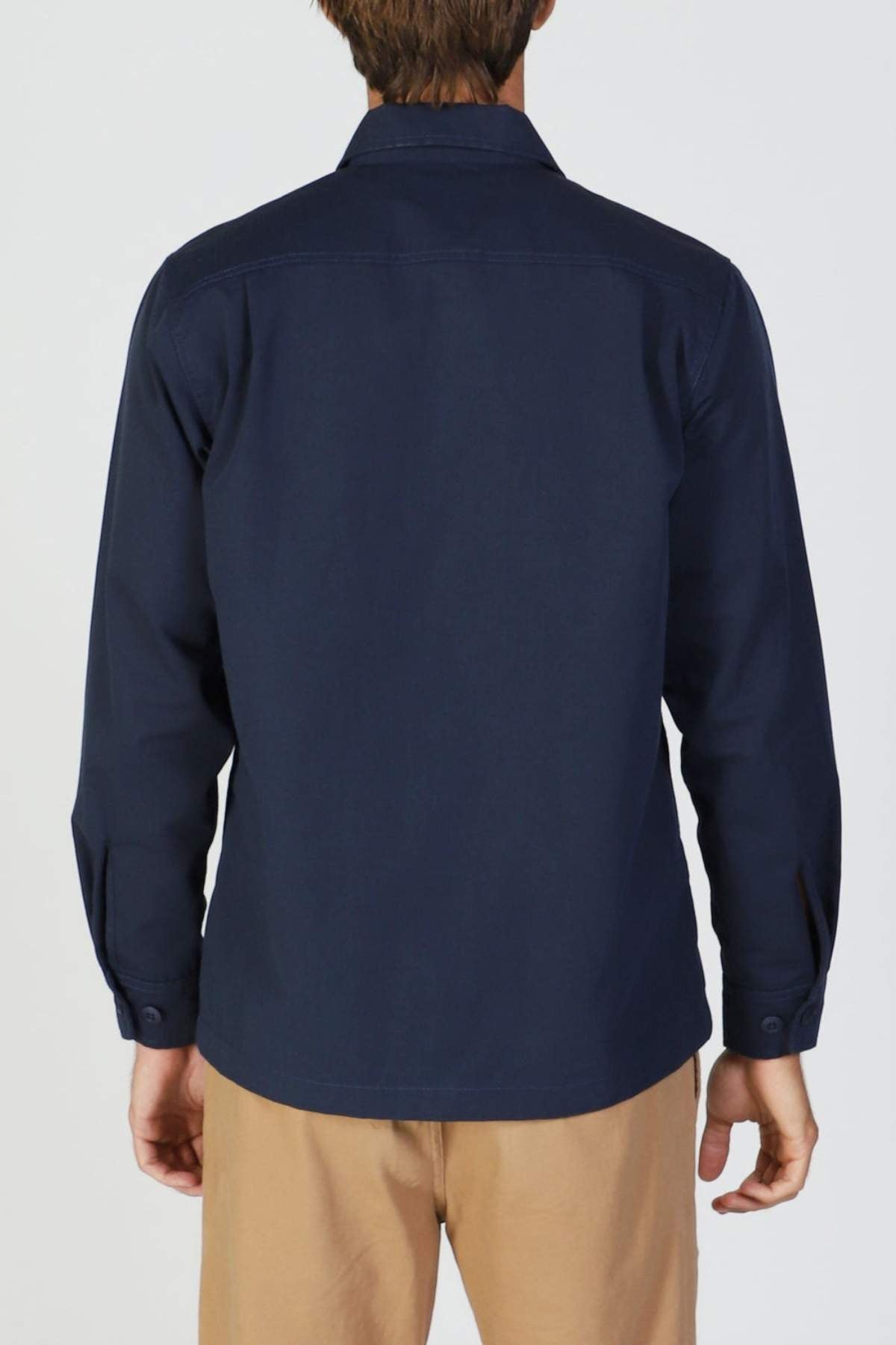 A person is shown from the back wearing a navy blue Mr Simple Ripstop Canvas Overshirt and light brown pants, standing against a plain light background.