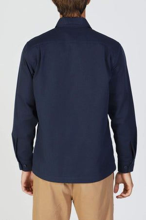 A person is shown from the back wearing a navy blue Mr Simple Ripstop Canvas Overshirt and light brown pants, standing against a plain light background.