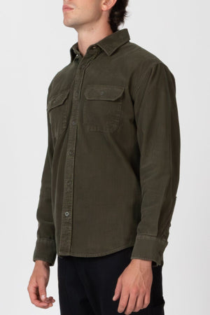 A person models the Mr Simple Sawyer Cord Shirt in long-sleeve olive green with front chest pockets, standing against a plain white background with their head slightly turned and face partially out of view.