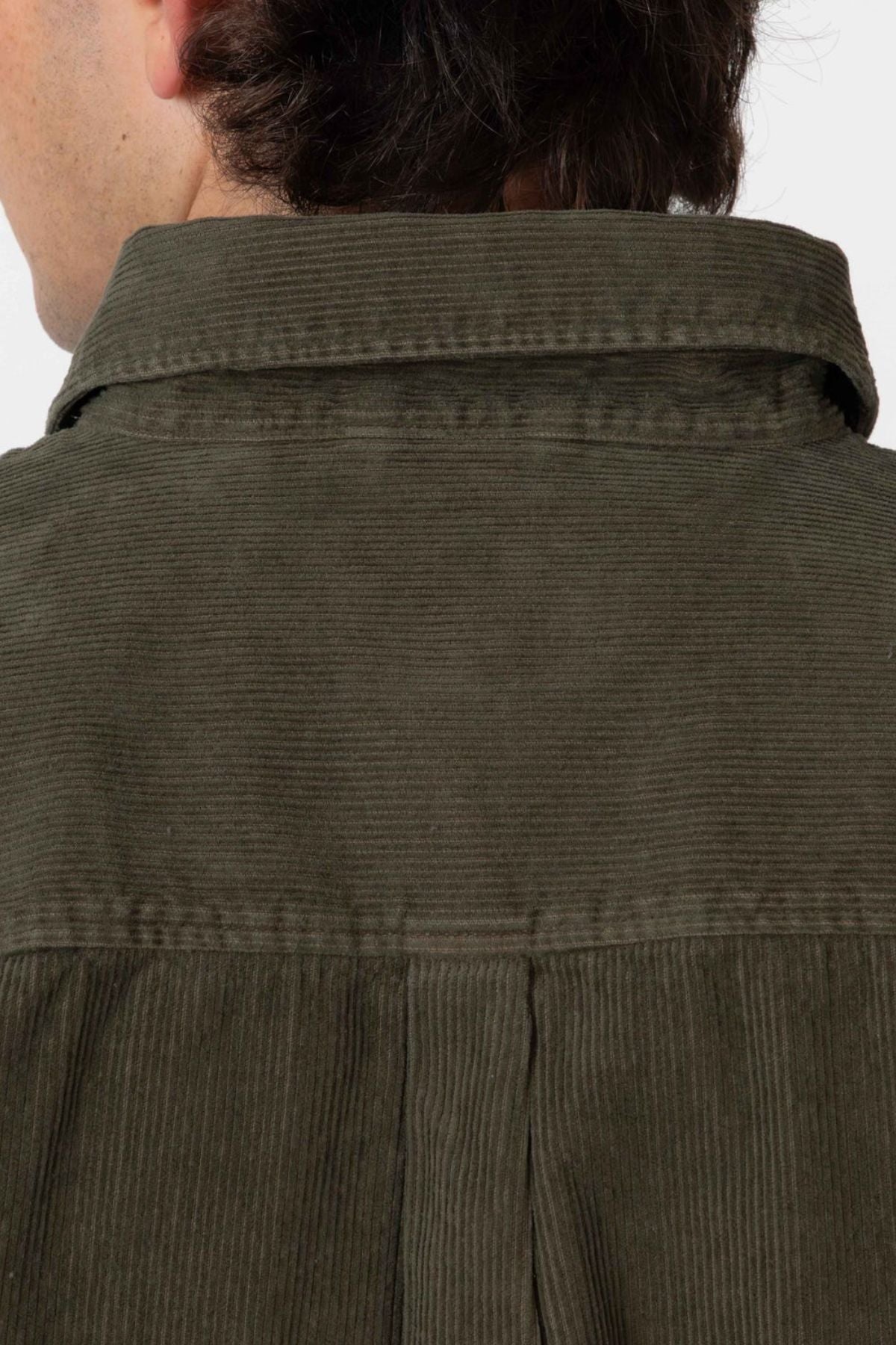 Close-up of the back of a person wearing the Mr Simple Sawyer Cord Shirt in olive green organic cotton, focusing on the collar and upper back, with only part of their head and hair visible.