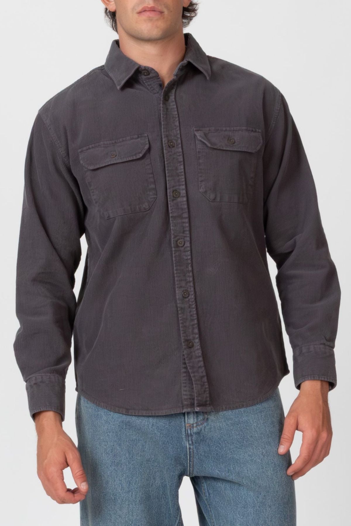 A person wears the Mr Simple Sawyer Cord Shirt, a dark gray, long-sleeve button-up with two chest pockets, paired with blue jeans and standing against a plain light background.