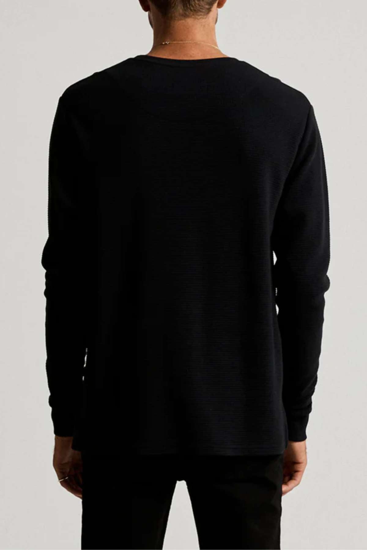 Wearing the Mr Simple Smith Waffle black long-sleeve shirt and matching pants, a person faces away from the camera. The plain, neutral background highlights the textured detail of their organic cotton outfit.