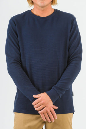 A person with light brown hair wears the Mr Simple Smith Waffle navy blue long sleeve organic cotton shirt and beige pants, standing against a plain white background with hands loosely clasped at the waist.