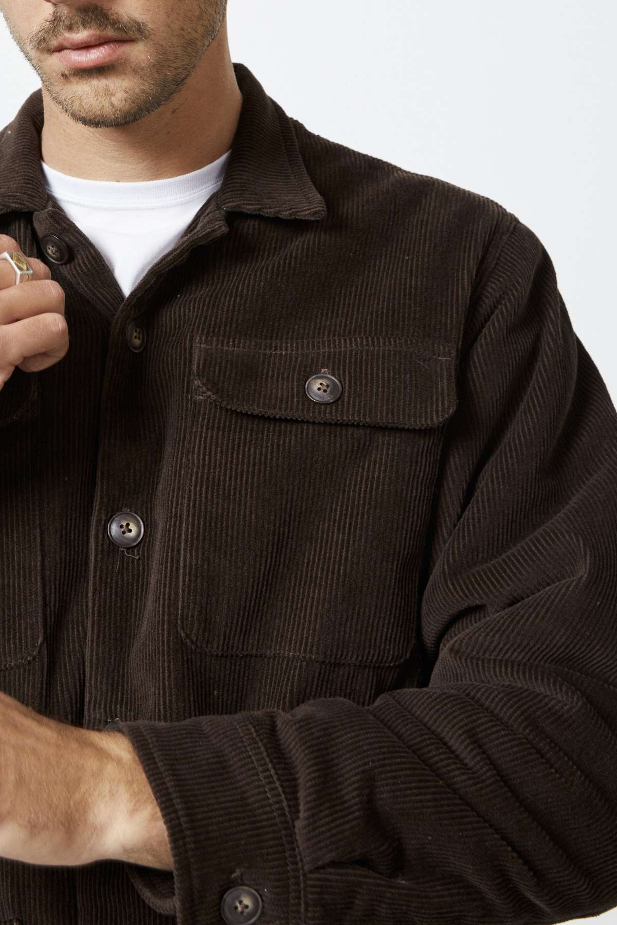 Someone wearing the Mr Simple Stockyard Sherpa Jacket, with its dark brown corduroy exterior and 100% cotton outer, adjusts their clothing. It features two large front pockets and button details, embodying casual sophistication from shoulders to waist.