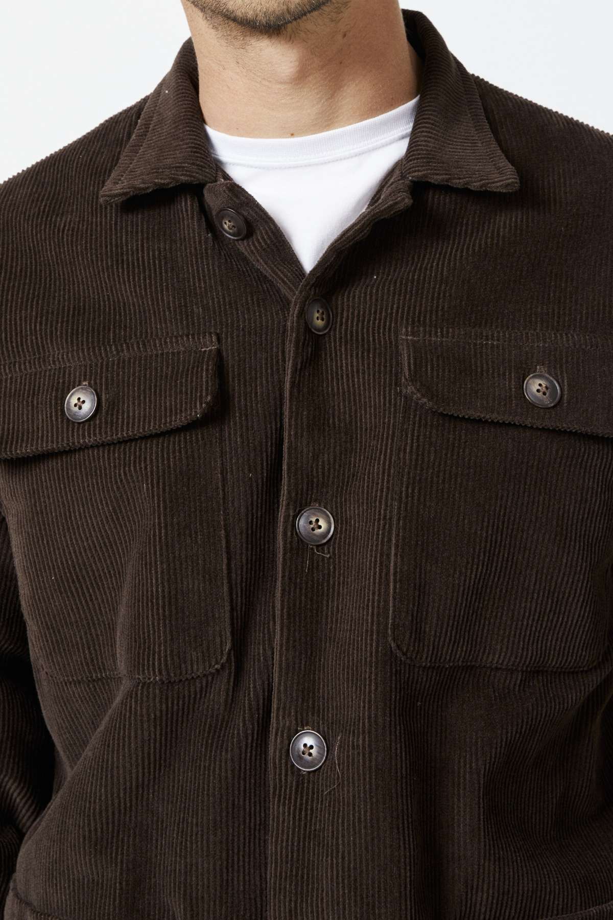 A person is wearing the Mr Simple Stockyard Sherpa Jacket, a dark brown corduroy piece with buttoned pockets over a white shirt, highlighting the texture and full button front design crafted from 100% cotton outer material.