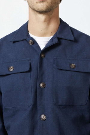 Close-up of a person wearing the Mr Simple Stockyard Sherpa Jacket in navy blue, featuring two buttoned chest pockets. The jacket is worn over a white undershirt. Only the lower part of the person's face is visible, suggesting a neutral expression.