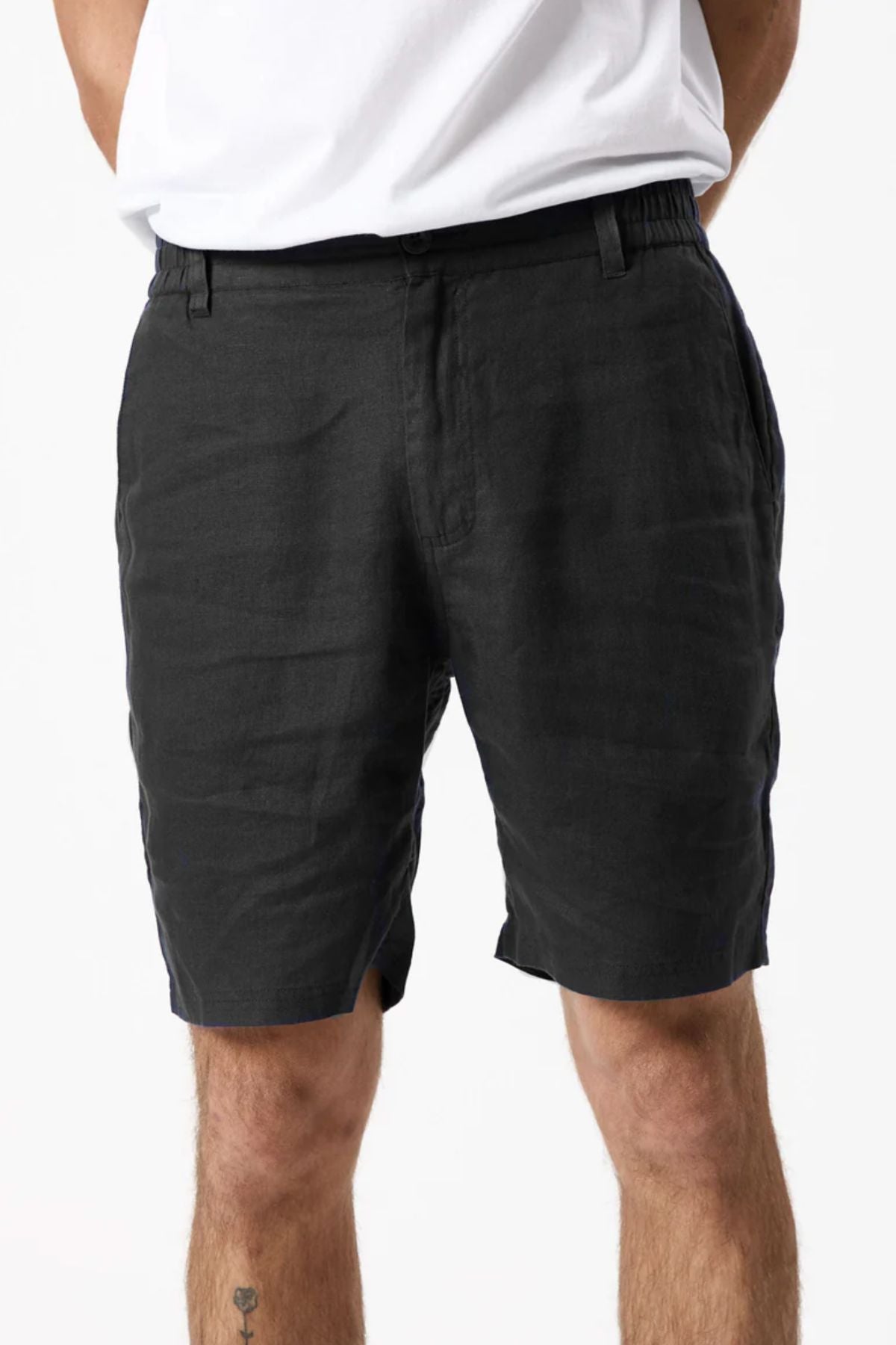 A person models the Mr Simple Tanner 3.0 Linen Short in black, showing a comfortable fit with hands behind their back. Only the lower torso and upper legs are visible, set against a plain white background.