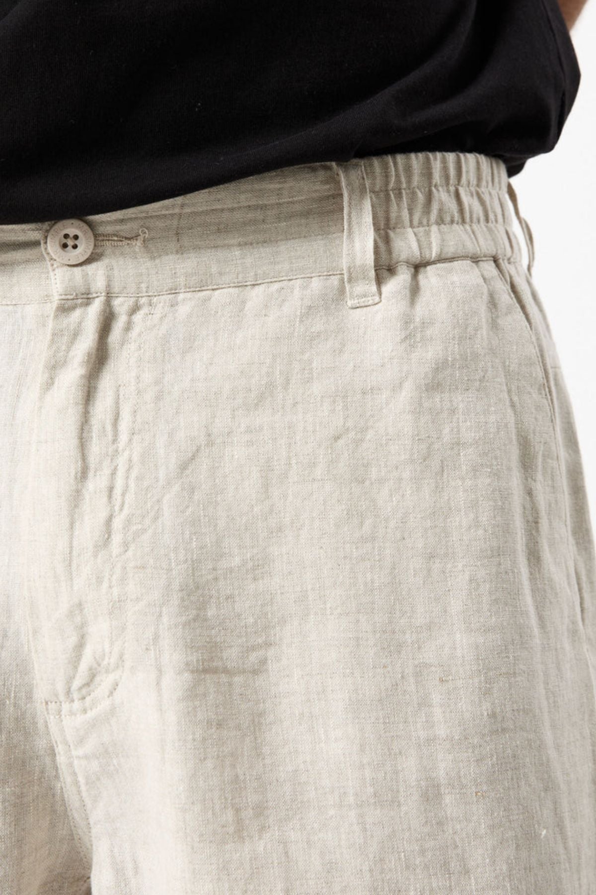Close-up of a person wearing the Mr Simple Tanner 3.0 Linen Short in light beige, featuring breathable fabric and an elastic waistband with button, paired with a black shirt.